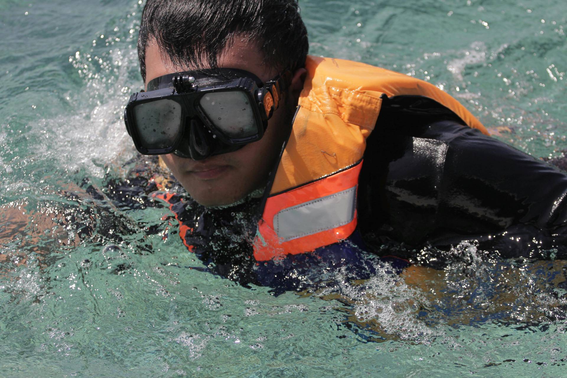 Person in a life jacket and goggles swimming in clear water.